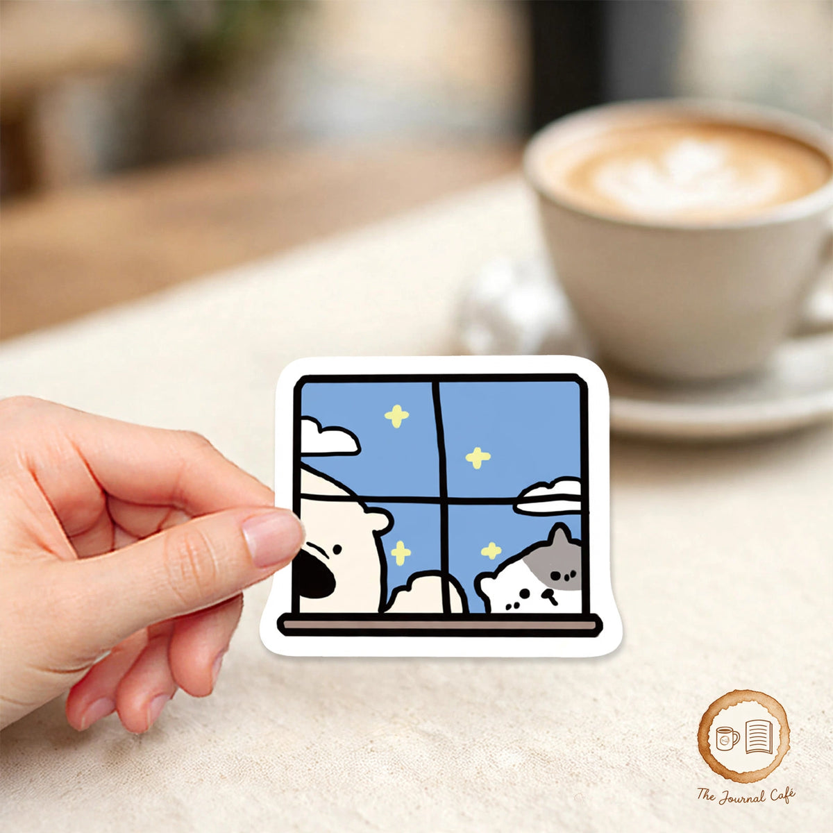 Cartoon Animal Hotel Stickers — cute bear and cat window sticker held over a cream café table, The Journal Café