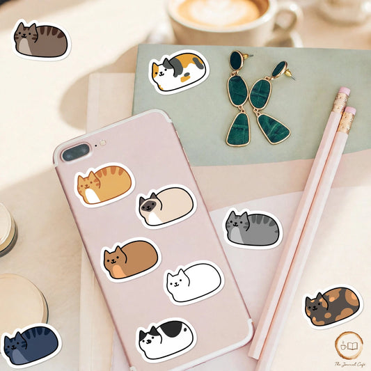 Personality cat stickers — cute loaf cat stickers in many colours styled on a cream café table, The Journal Café