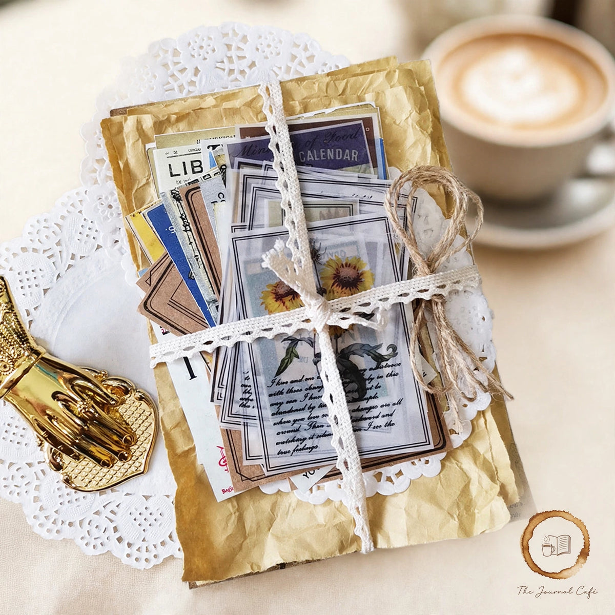 Junk Journal Retro Material Pack — mixed vintage ephemera papers tied with lace styled on a cream café table, The Journal Café