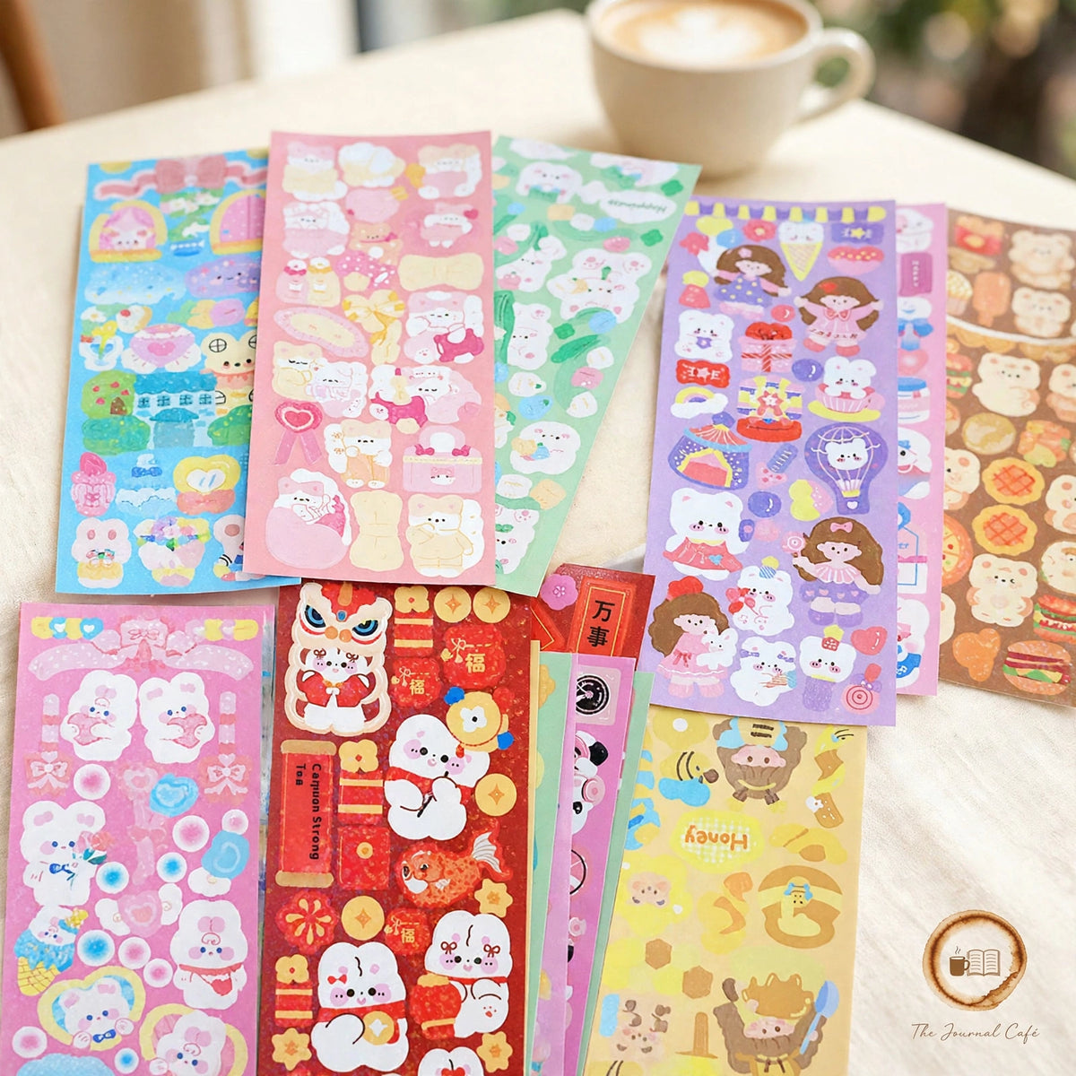 Holographic Laser Sticker Sheets — ten colorful kawaii sticker sheets fanned across a cream café table, The Journal Café