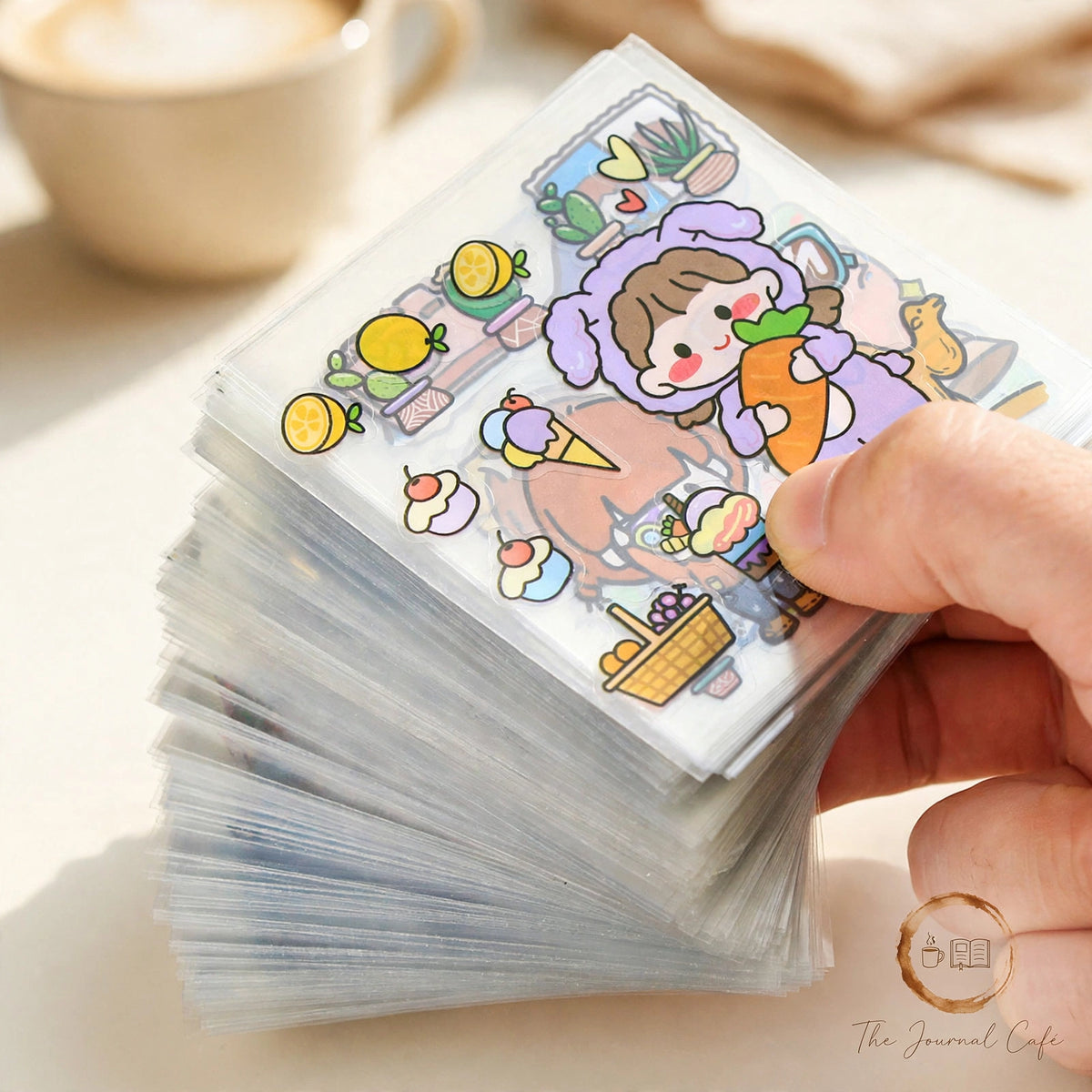 Non-Duplicate PET Journal Stickers — stack of clear PET sticker sheets with cute dessert and character designs styled on a cream café table, The Journal Café